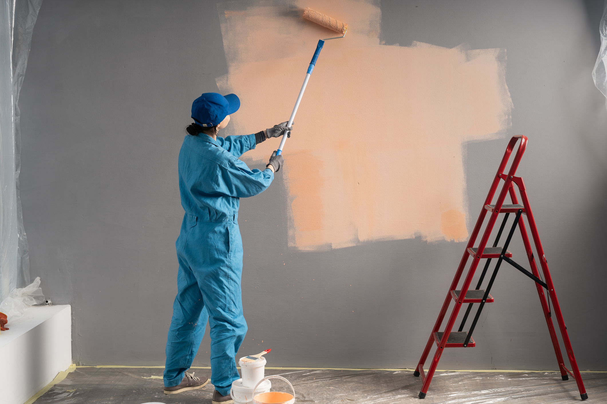 Builder or painter in cap Paints walls with long painting roller. business, building, renovation and people concept